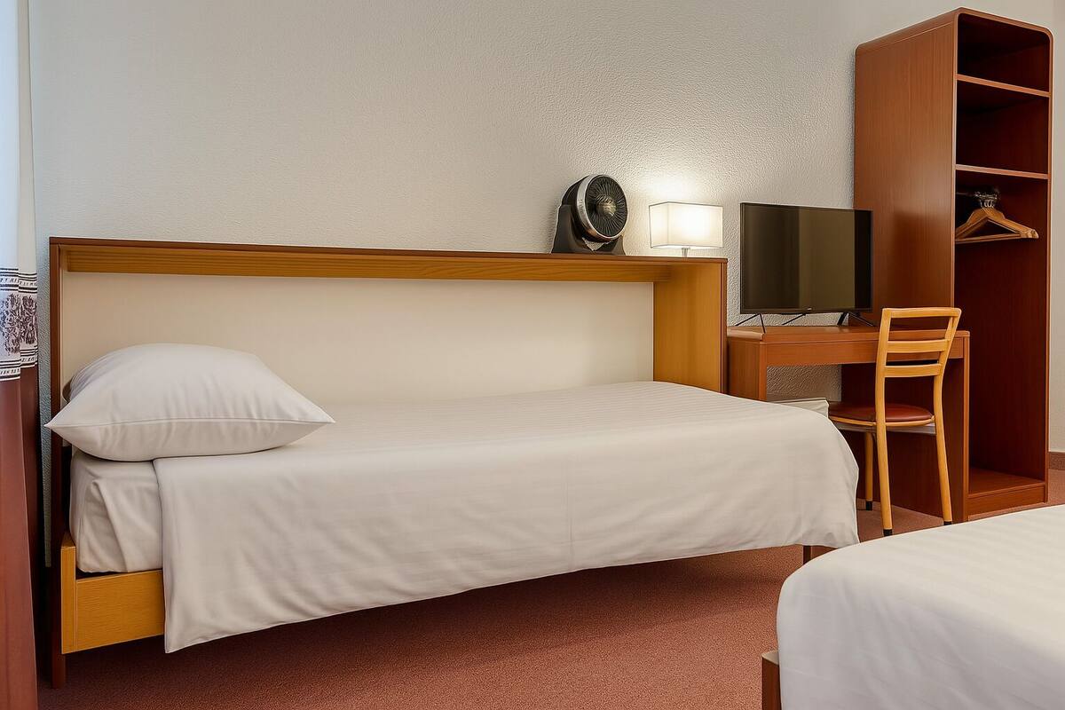 Une chambre d’hôtel avec un lit simple, un bureau avec une chaise, une télévision et une armoire.
