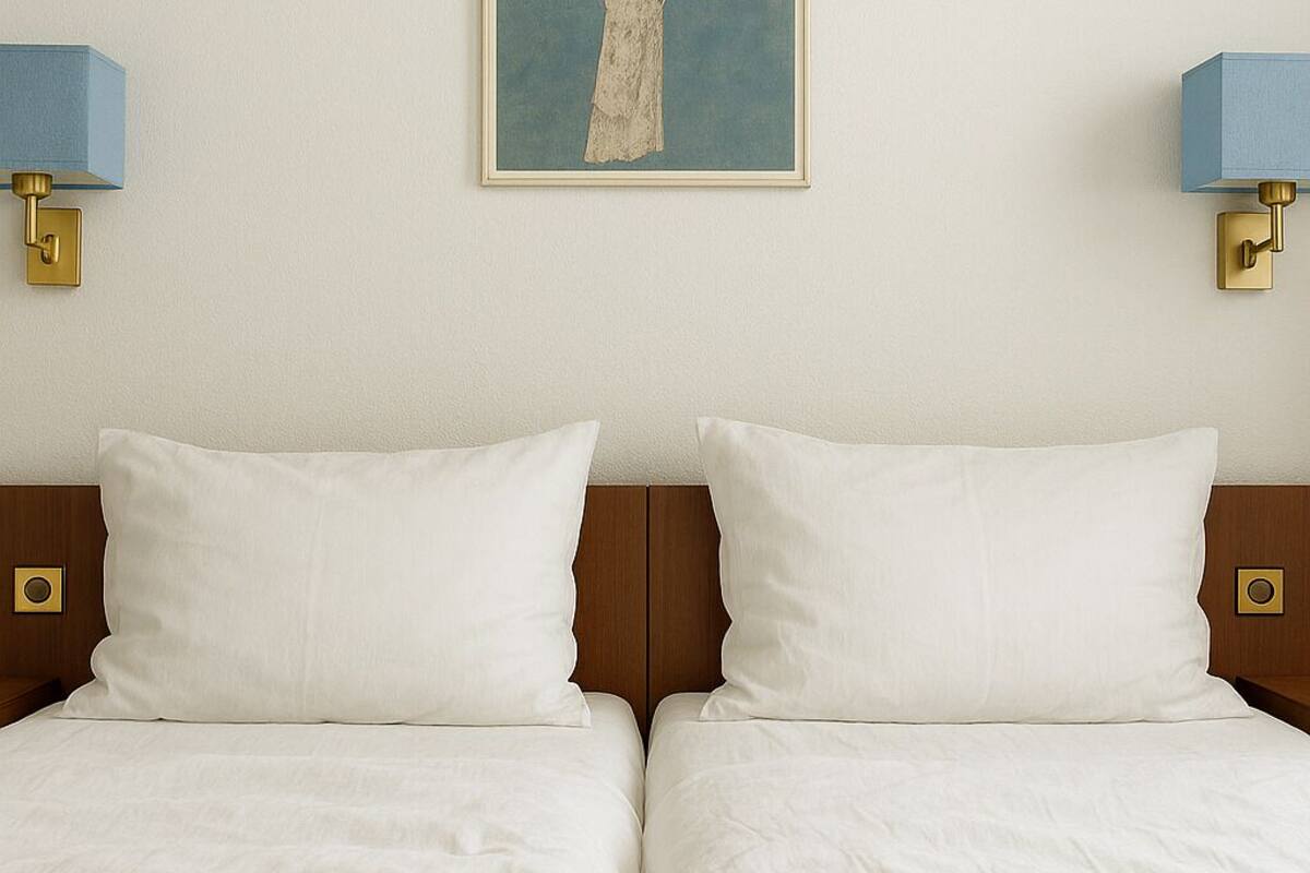 Un lit double avec du linge de lit blanc, une œuvre d’art encadrée au-dessus, et deux lampes fixées au mur.