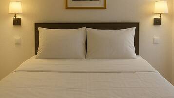A hotel room with a bed, two wall-mounted lamps, and a framed picture on the wall.