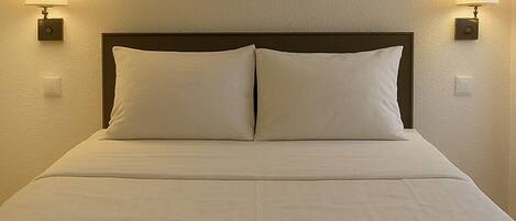 Een hotelkamer met een bed, twee wandlampen en een ingelijst foto aan de muur.