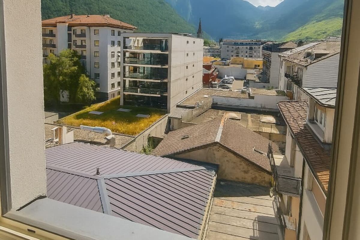 Une vue depuis une fenêtre donnant sur une ville, avec ses bâtiments, une montagne et un ciel dégagé.