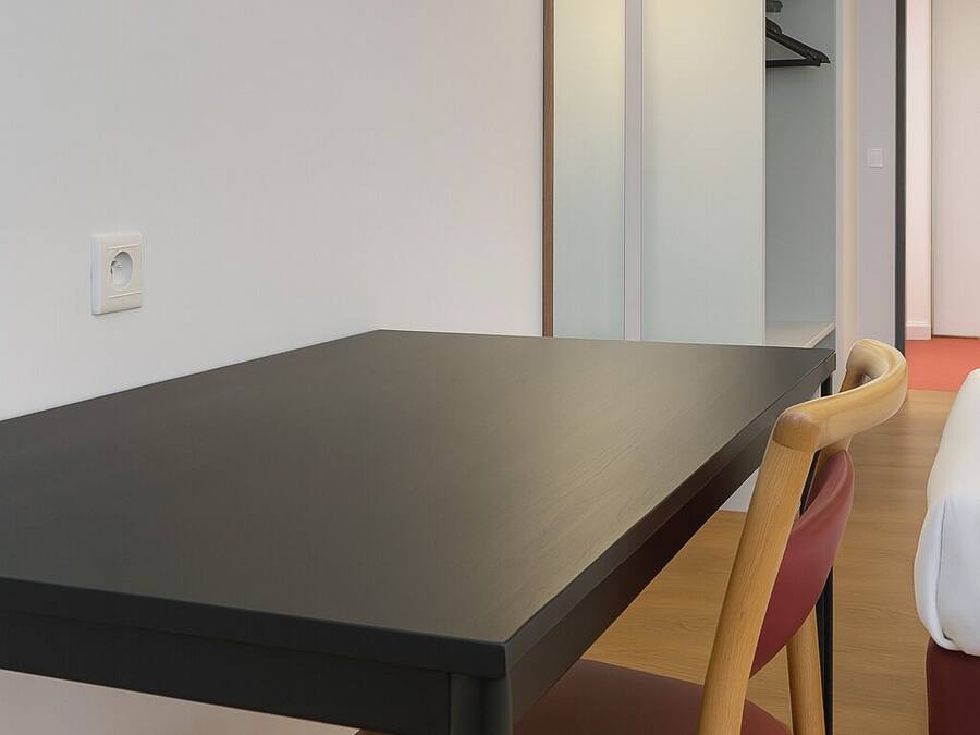 Una habitación moderna con una mesa de madera oscura, una silla tapizada en rojo y un aplique de pared.