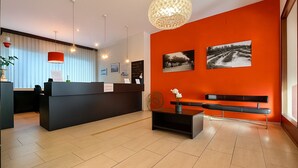 Un espace d’accueil avec un comptoir noir, un banc et deux photographies encadrées accrochées au mur.