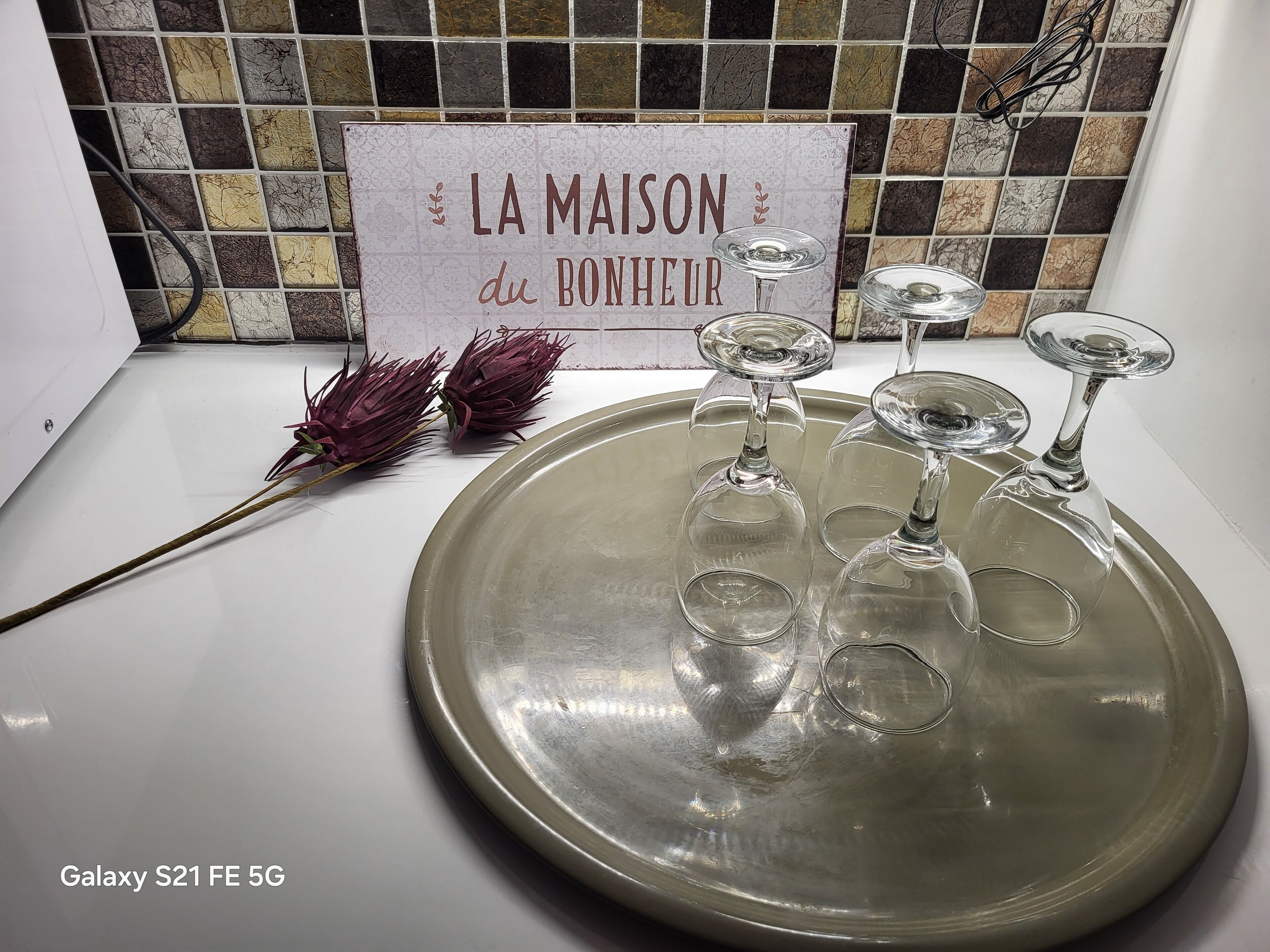 A kitchen counter with a sign reading "LA MAISON du BONHEUR" and four wine glasses on a tray.