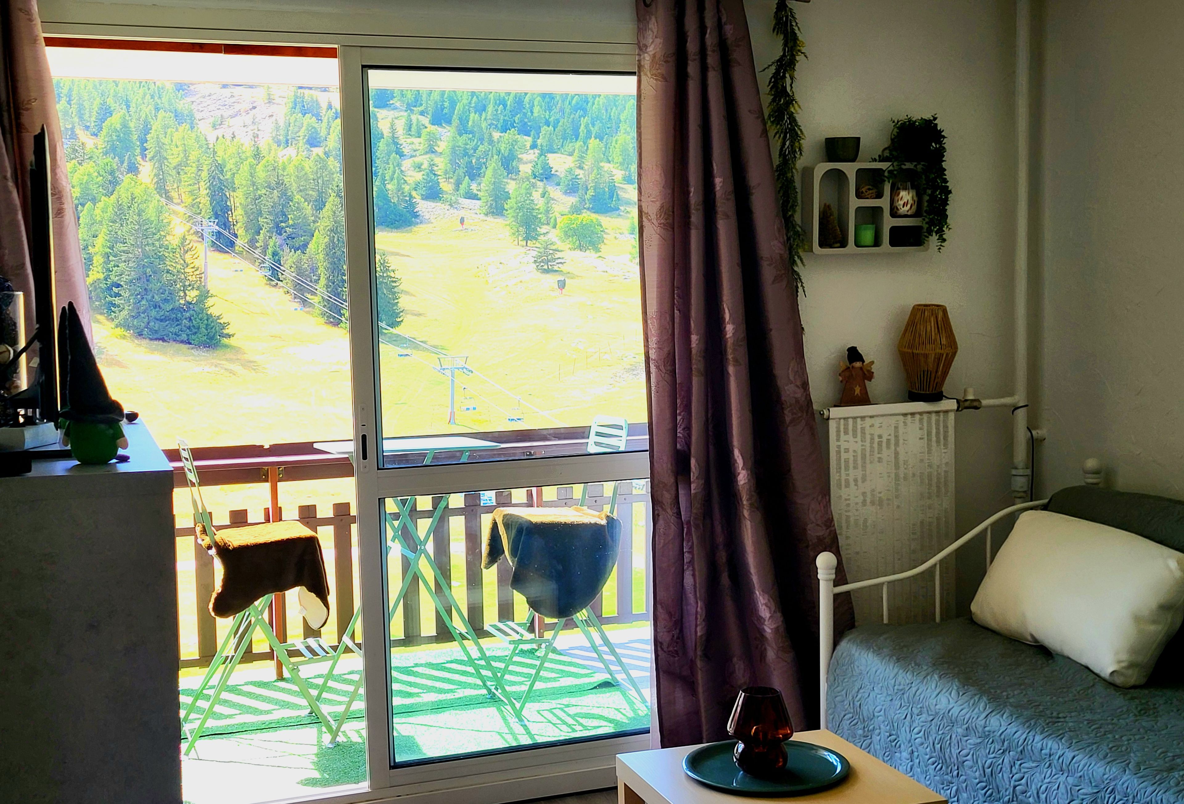 Una habitación con balcón, una cama, una mesita con un jarrón y vistas a una zona boscosa.
