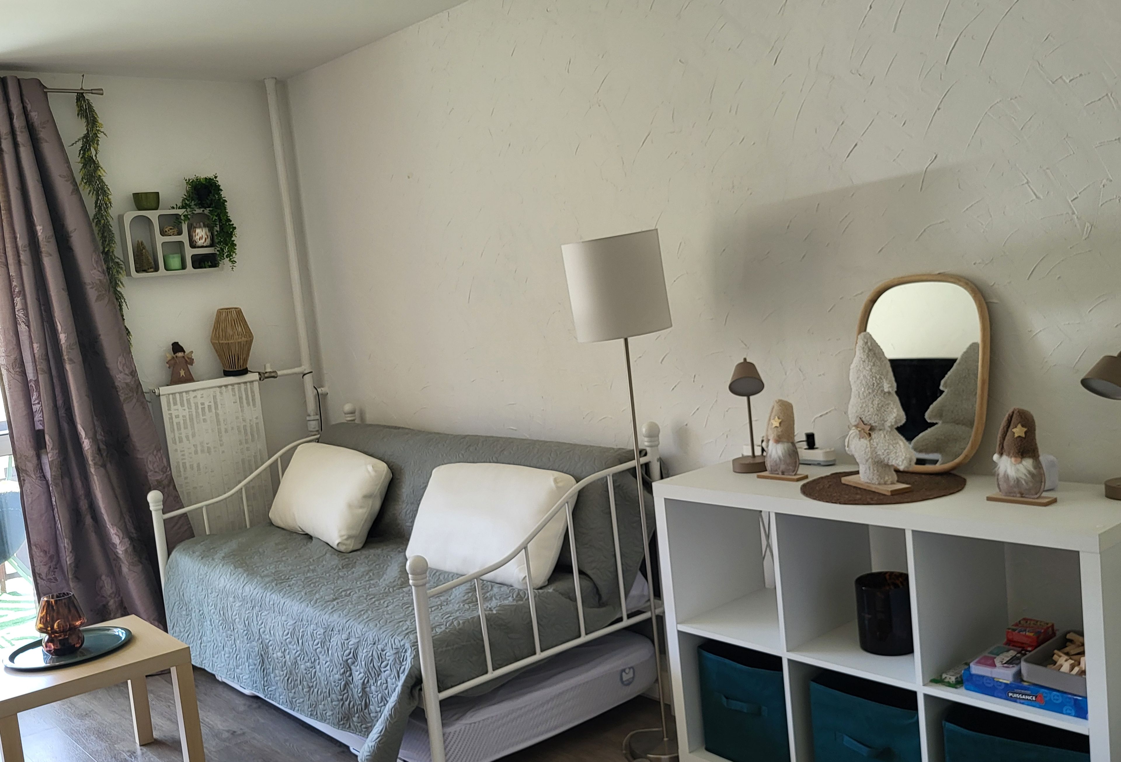 A bedroom with a bed, bedside table, lamp, mirror, and storage shelves.