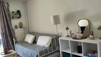 A bedroom with a bed, bedside table, lamp, mirror, and storage shelves.