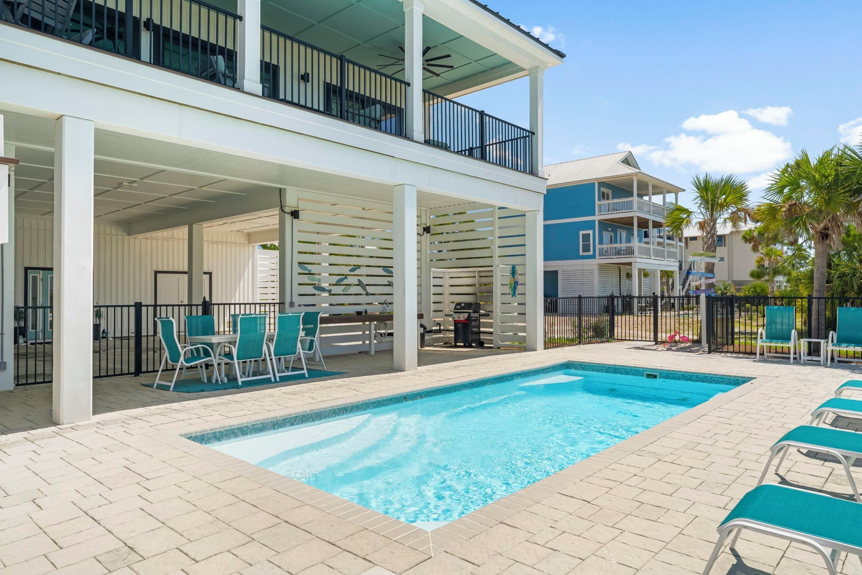 A pool area with a clear blue pool, outdoor seating, and a covered patio.