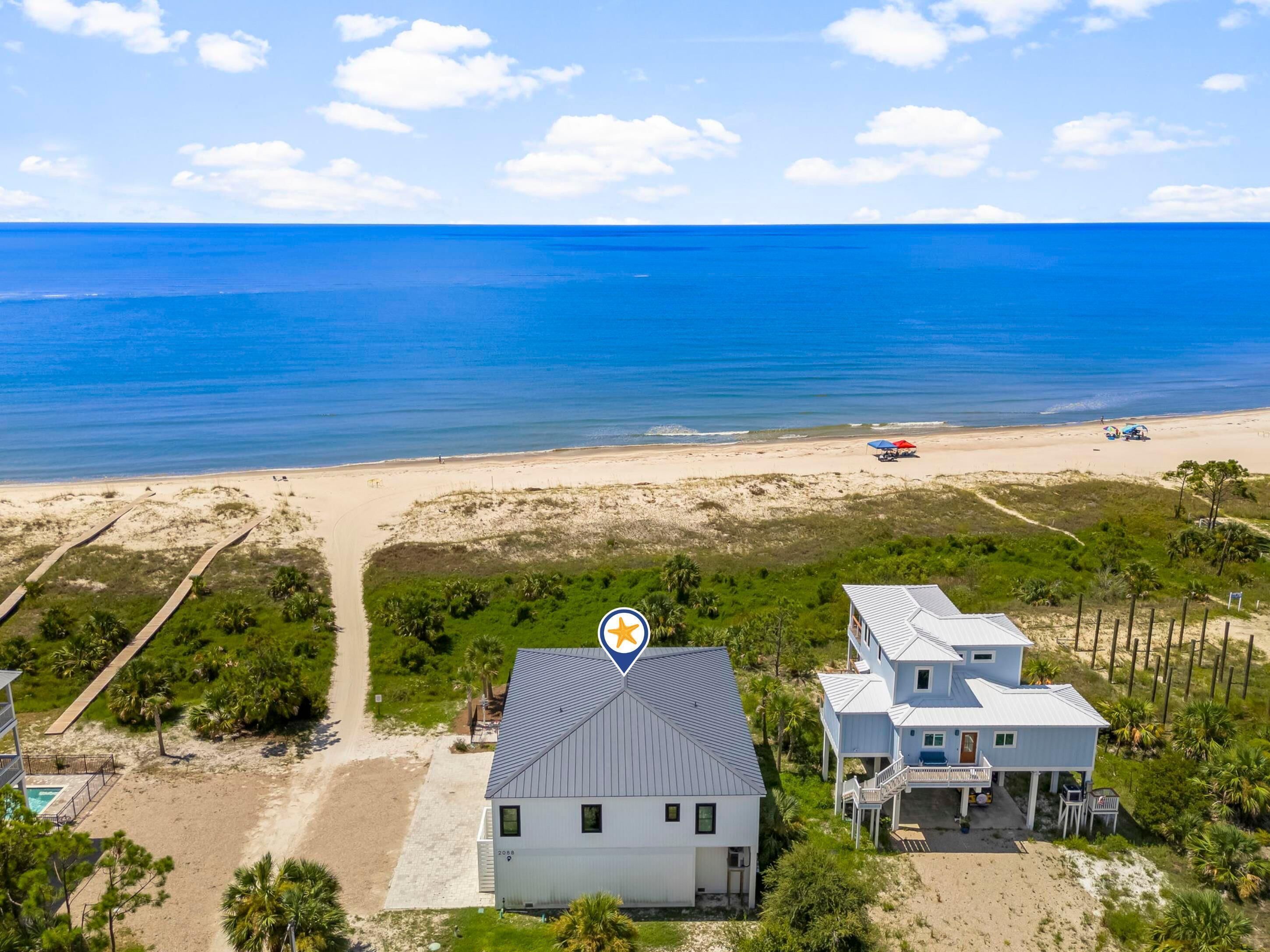 A coastal property with a beach view, a paved pathway, and a house with a balcony.
