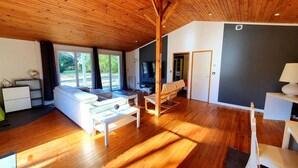 A spacious living area with a wooden ceiling, a sofa, a coffee table, and a TV. - Guesthouse in wooded grounds (Saint-Vincent-de-Tyrosse)
