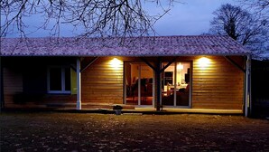 A wooden cabin with a covered porch and a sliding glass door entrance. - Guesthouse in wooded grounds (Saint-Vincent-de-Tyrosse)