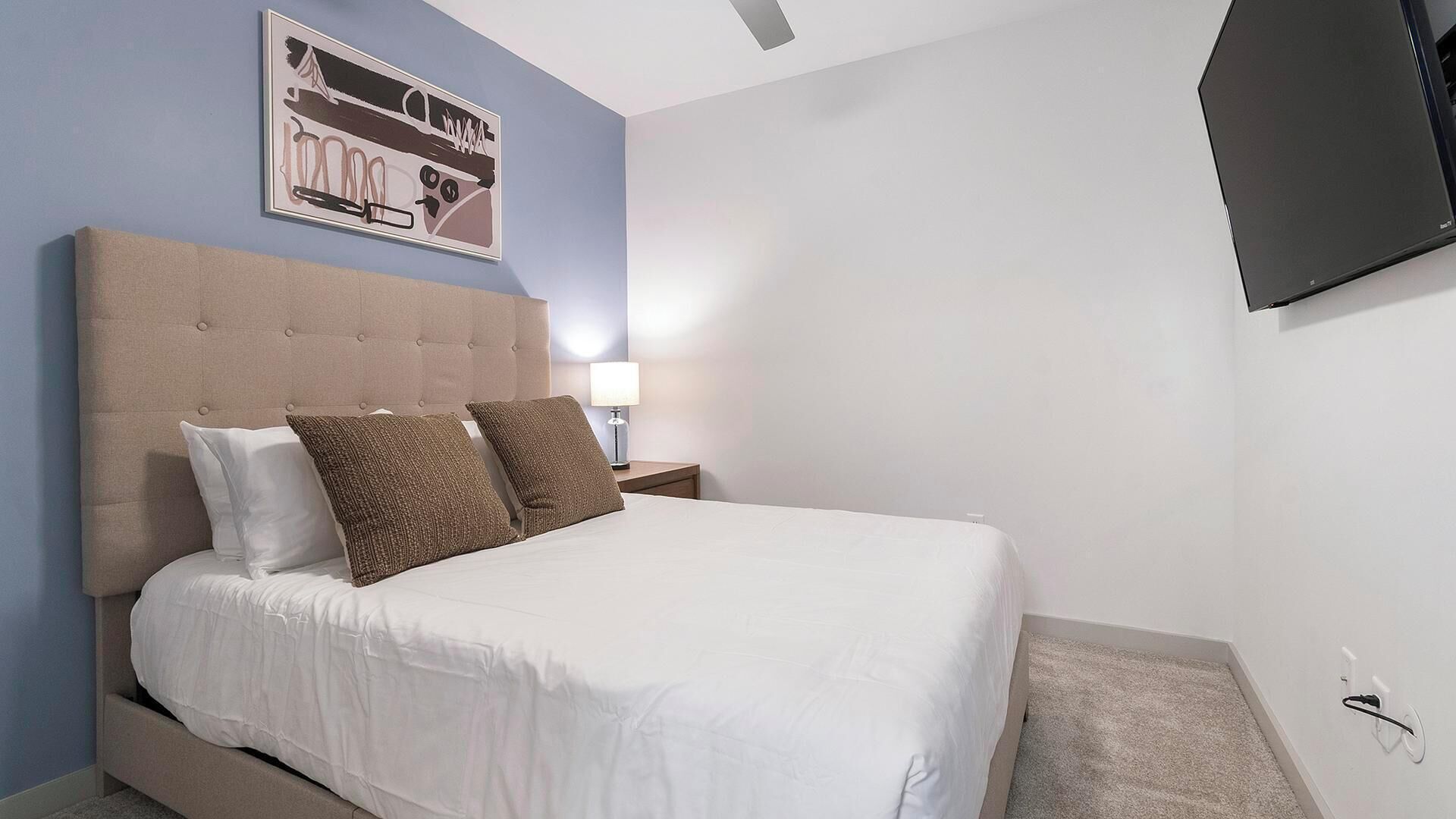 Un lit bien fait, avec une literie blanche et marron, une tête de lit capitonnée et un tableau encadré accroché au mur.