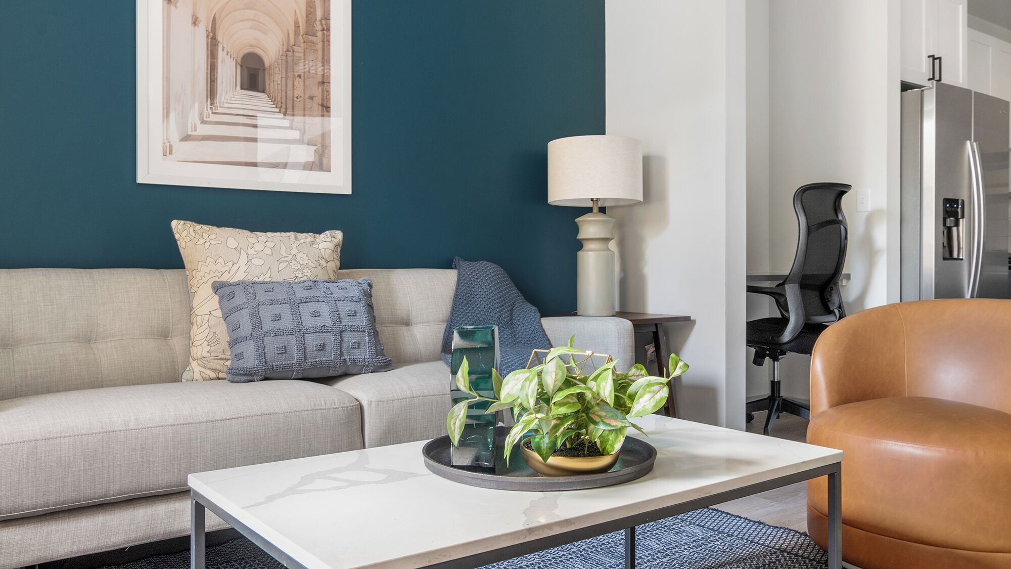A modern living room with a sofa, a coffee table with plants, a lamp, and a refrigerator.