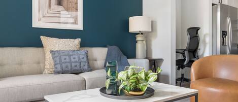 A modern living room with a sofa, a coffee table with plants, a lamp, and a refrigerator.