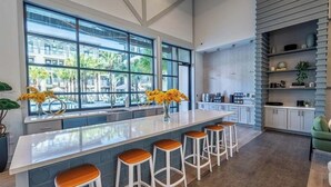 A modern kitchen with a large island, bar stools, and a view of palm trees through large windows. - Historic Springfield Apartments by Landing (Jacksonville)