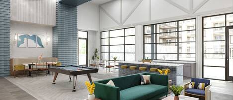 A spacious lobby with a pool table, green sofa, and bar area.