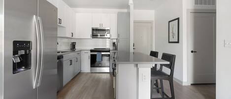 A modern kitchen with stainless steel appliances, white cabinetry, and a central island with seating.