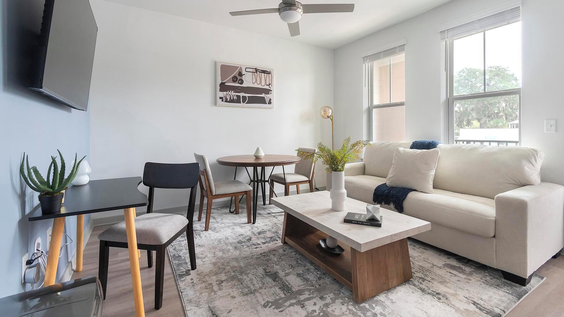A modern living room with a sofa, coffee table, chairs, a small table, and a ceiling fan.