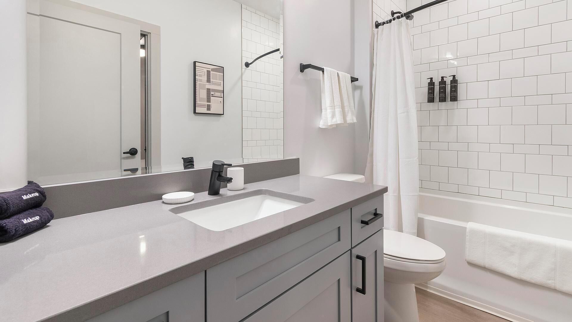 A modern bathroom with a white sink, dark-toned vanity, a large mirror, and a shower area.