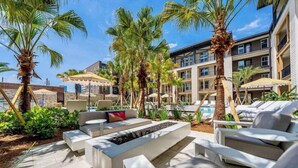 A poolside area with lounge chairs, a fire feature, and palm trees. - Historic Springfield Apartments by Landing (Jacksonville)