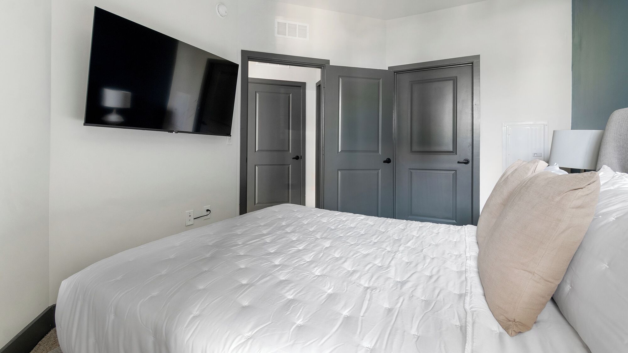 A bedroom with a bed, a TV mounted on the wall, and two doors.