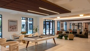 A modern indoor space with a pool table, comfortable seating, large windows, and a wooden ceiling. - Southbank Apartments by Landing (Jacksonville)