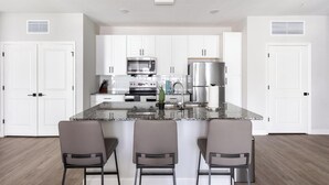 Une cuisine moderne avec des meubles blancs, un plan de travail en granit et trois tabourets de bar.