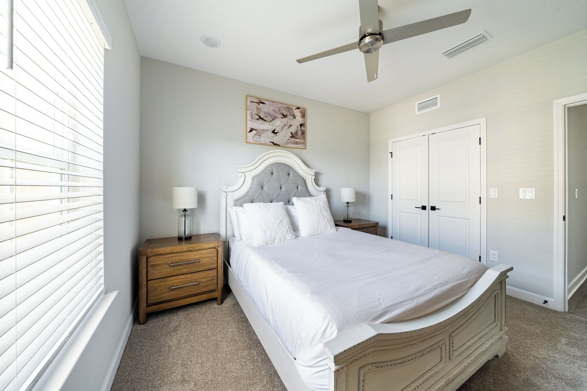 A bedroom with a bed, nightstands, a ceiling fan, a painting, and a set of double doors.