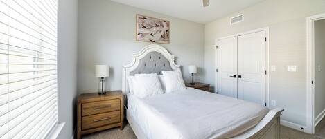 A bedroom with a bed, nightstands, a ceiling fan, a painting, and a set of double doors.