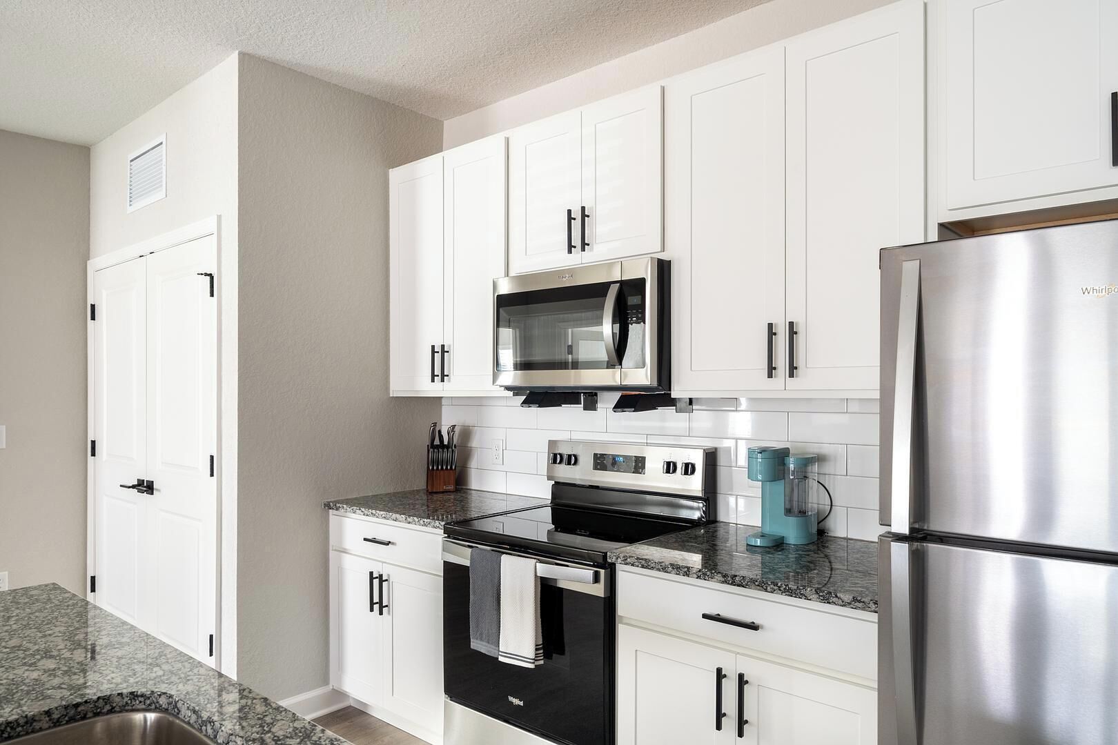 A modern kitchen with white cabinets, stainless steel appliances, a microwave, oven, and a refrigerator.