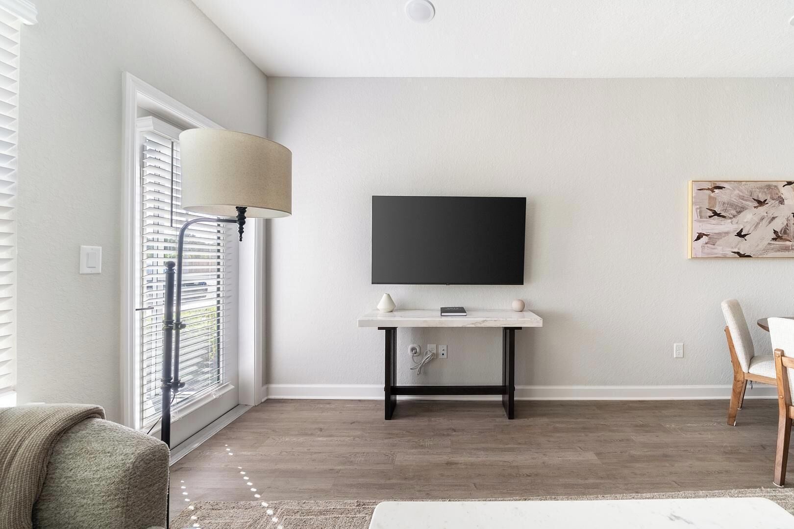 A modern living room with a flat-screen TV mounted on the wall, a white console table, a lamp, and a chair.