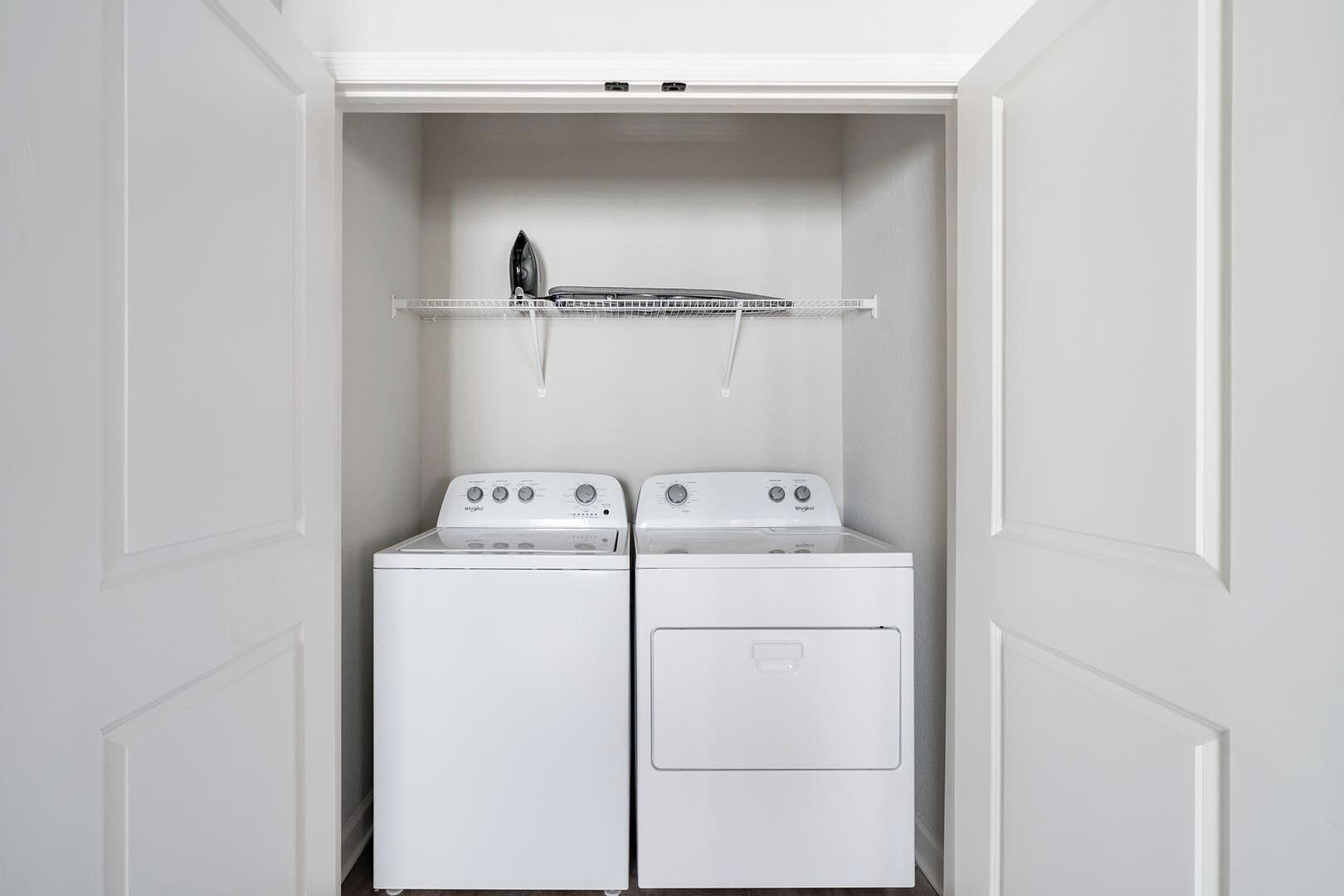 Une buanderie équipée de deux machines à laver et deux sèche-linge Whirlpool blancs, d’un étendoir métallique et d’une porte blanche.