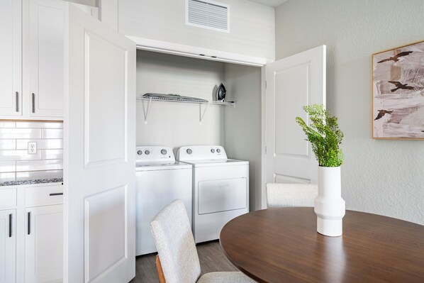 A compact kitchen with white appliances, a dining table, and a potted plant.