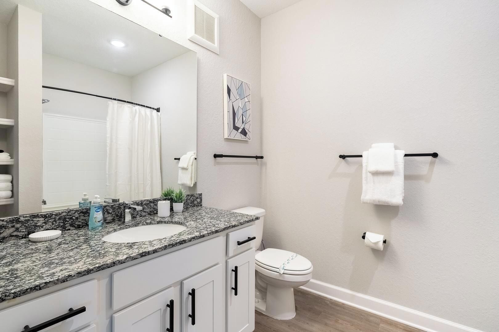 A bathroom with a granite countertop, a white sink, a toilet, and a towel rack.