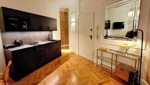 A modern kitchen with dark cabinets, a wooden herringbone floor, a glass coffee table, and a mirror above the sink. - TALISMANO LUXURY MAISON (Napoli)