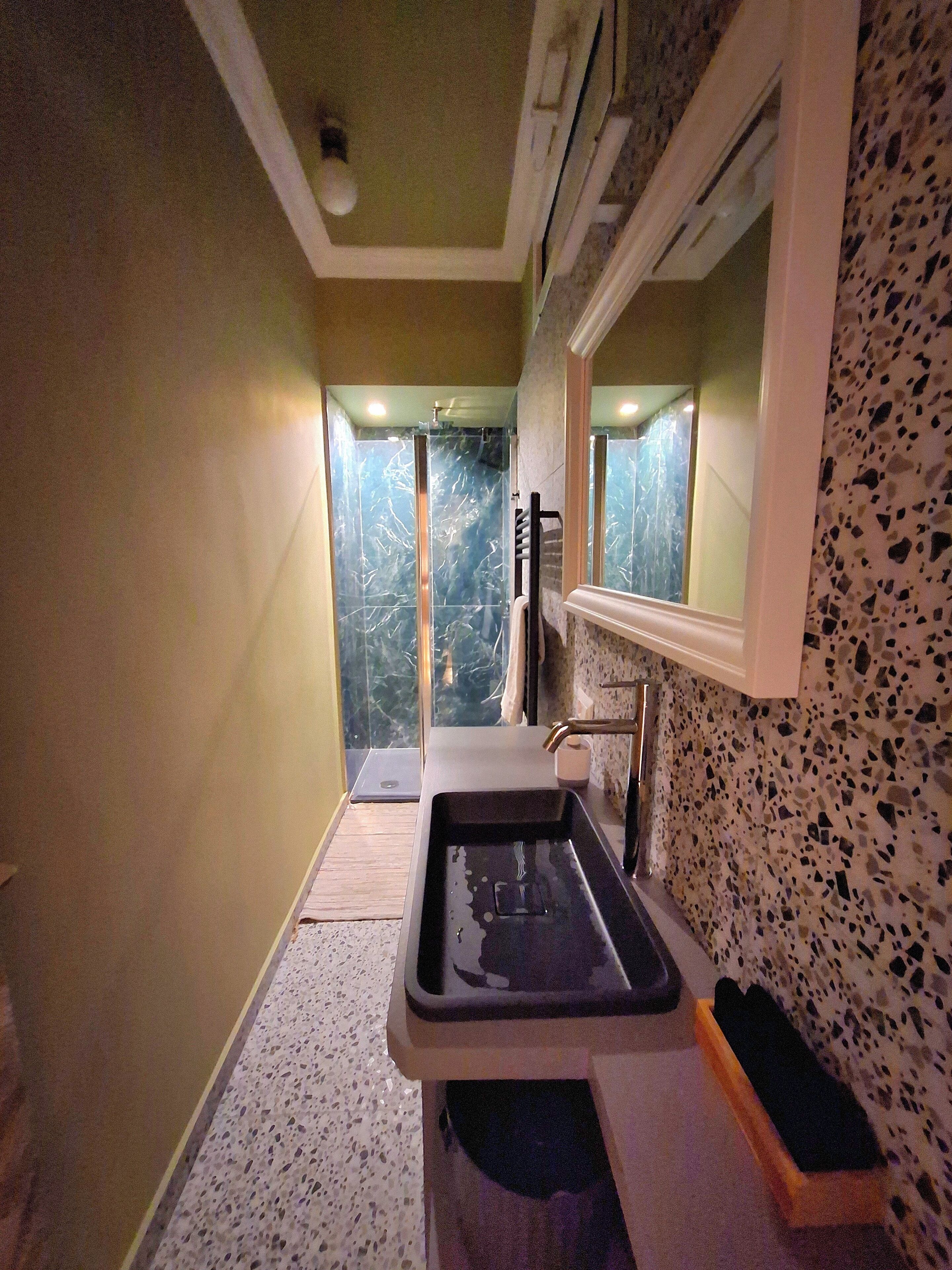 A narrow bathroom with a sink, a mirror, and a shower area.