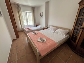 A hotel room with two beds, a wooden wardrobe, and a window with curtains. - Comfort Apartment El Mar (Sveti Stefan)