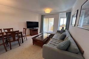 Uma sala de estar com sofá, mesa de centro, televisão e um espaço de refeições com cadeiras e mesa.