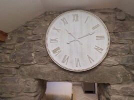 Un reloj de pared grande y rústico con números romanos montado sobre una pared de piedra.