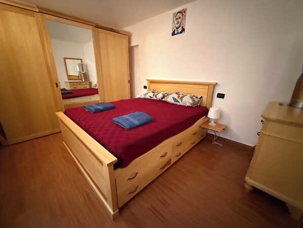 A bedroom with a wooden bed, a nightstand, a dresser, and a mirror.