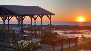Un gazebo in legno con tetto, affacciato su una spiaggia con il sole al tramonto.