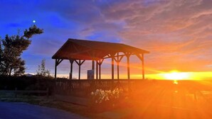 Un gazebo con tetto e lati aperti, circondato da alberi e una recinzione, al tramonto.