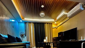 A modern living room with a wooden floor, a sofa, a TV, and a ceiling with a unique design. - IV’s Condo with AC, WiFi, Netflix in Cainta (Cainta)