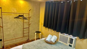 A hotel room with a bed, a small stool, a drying rack, and a wall-mounted air conditioner. - IV’s Condo with AC, WiFi, Netflix in Cainta (Cainta)