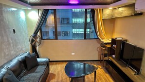 A modern living room with a leather sofa, a glass coffee table, a flat-screen TV, and a large window with curtains. - IV’s Condo with AC, WiFi, Netflix in Cainta (Cainta)