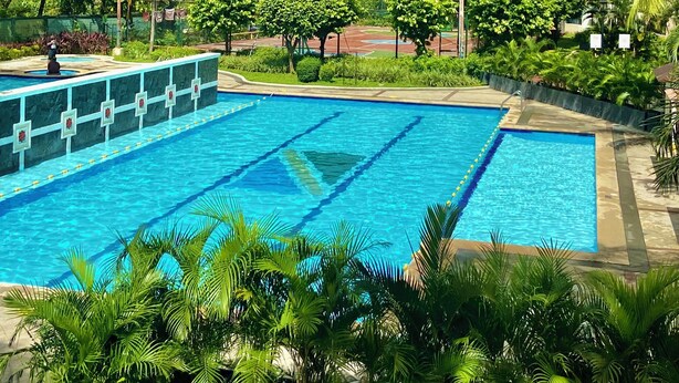 A swimming pool with clear blue water, surrounded by lush greenery and a tall building in the background. - IV’s Condo with AC, WiFi, Netflix in Cainta (Cainta)