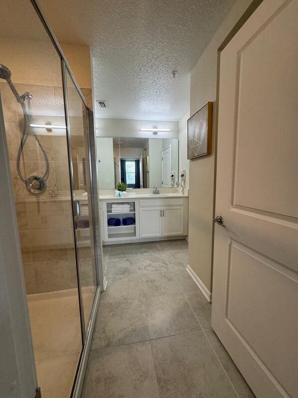 A bathroom with a glass shower enclosure, a white sink, and a large mirror.