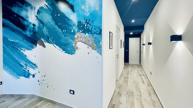A hallway with a large abstract mural on the left wall, a wooden floor, and recessed lighting on the ceiling. - Nautilus B & B  (Scalea)
