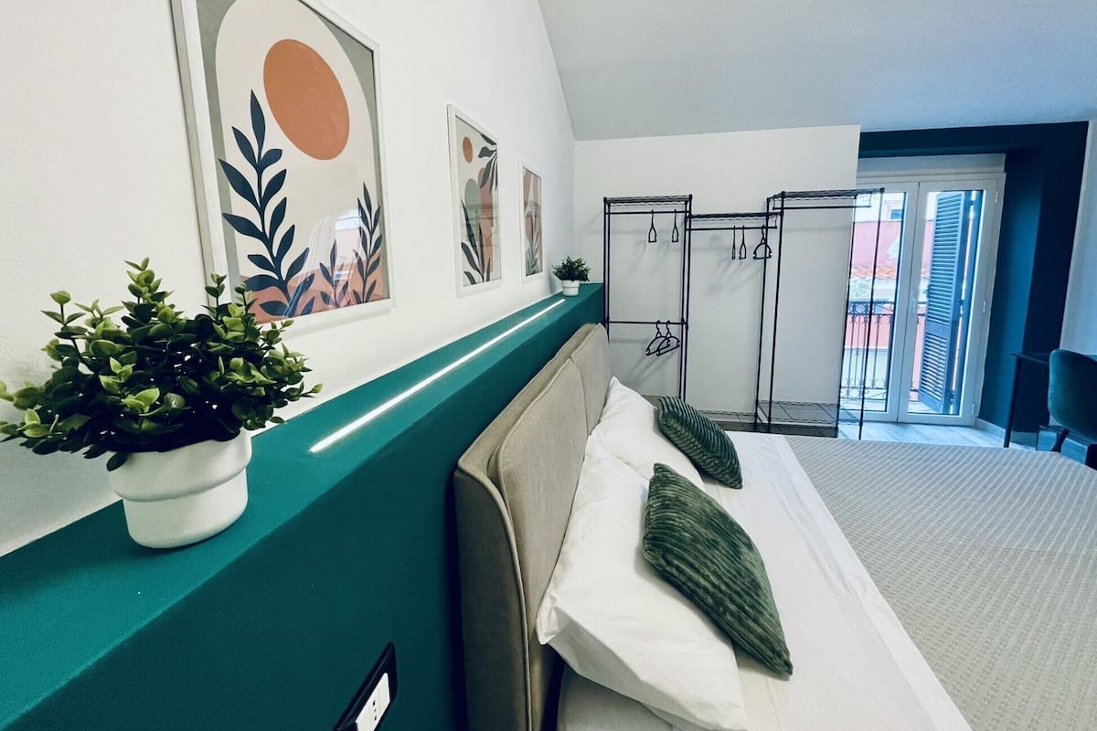 A hotel room with a bed, a green accent wall, a potted plant, and artwork.