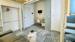 A modern living room with a sofa, a coffee table with a plant, a TV on the wall, and a staircase leading to a loft area. - Nautilus B & B  (Scalea)